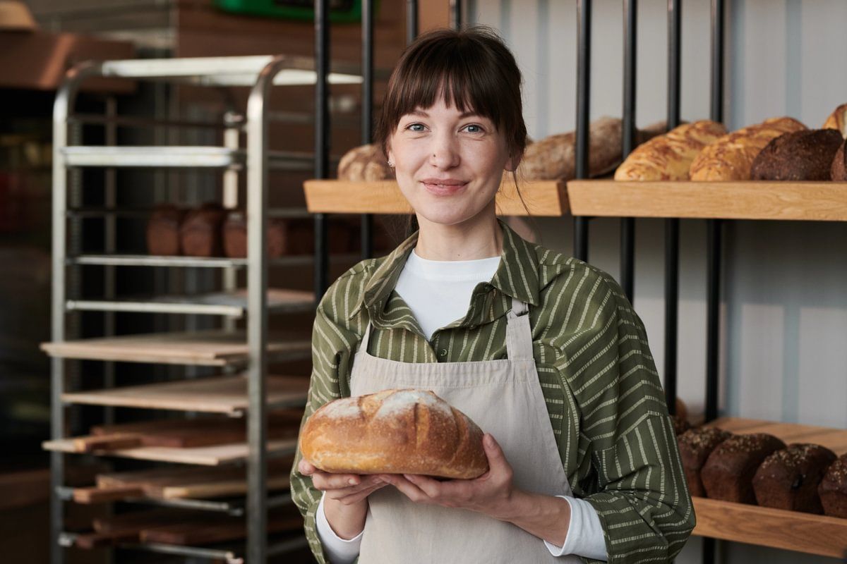 a woman is holidng a loaf of bread in a bekery kitchen