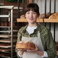 a woman is holidng a loaf of bread in a bekery kitchen