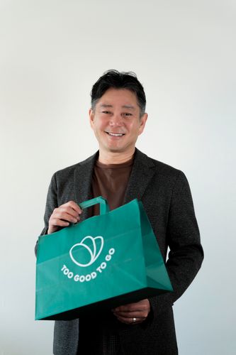 a man in a grey shirt is smiling in front of a green background