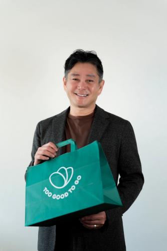 a man in a grey shirt is smiling in front of a green background