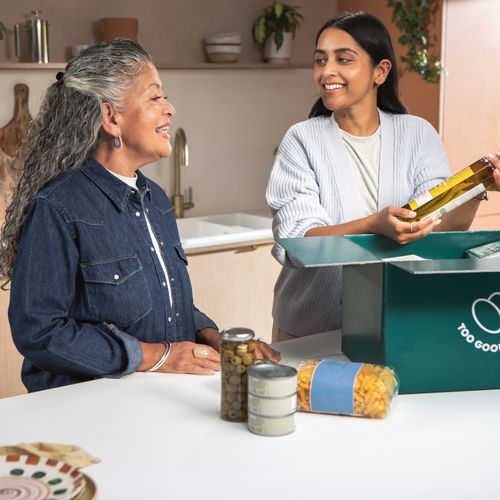 a woman is holding a bottle of olive oil next to an older woman in a kitchen .