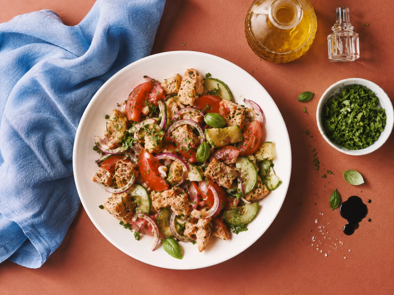 Panzanella salad with tomatoes, cucumbers, red onion, croutons, and basil in a white bowl.