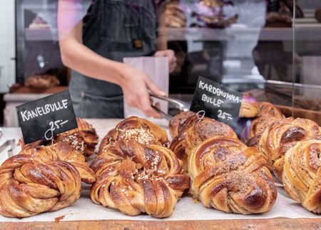Swedish cinnamon and cardamom buns on display in a bakery, with a person behind the counter.