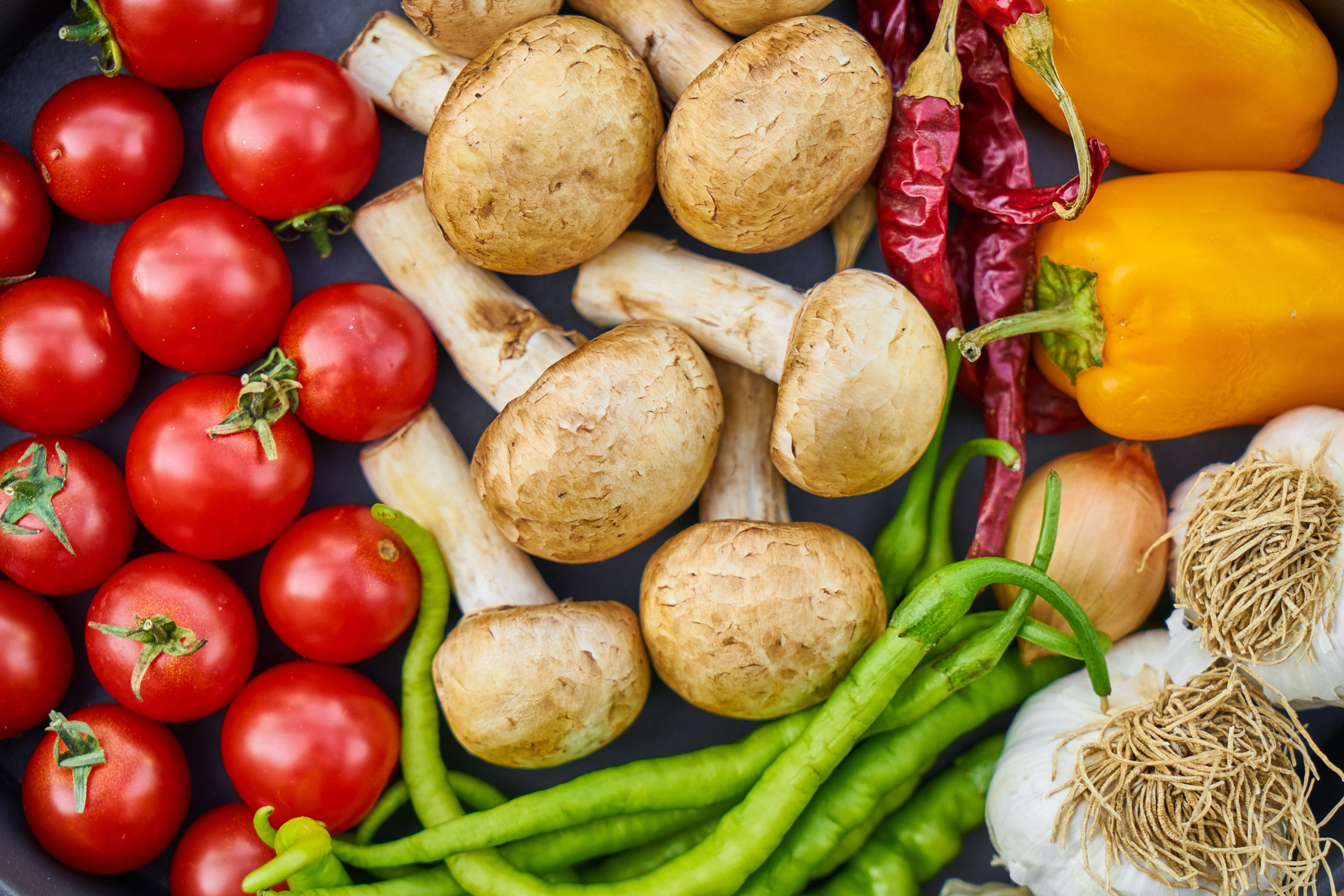 a pan filled with tomatoes , mushrooms , peppers , onions , garlic and other vegetables .