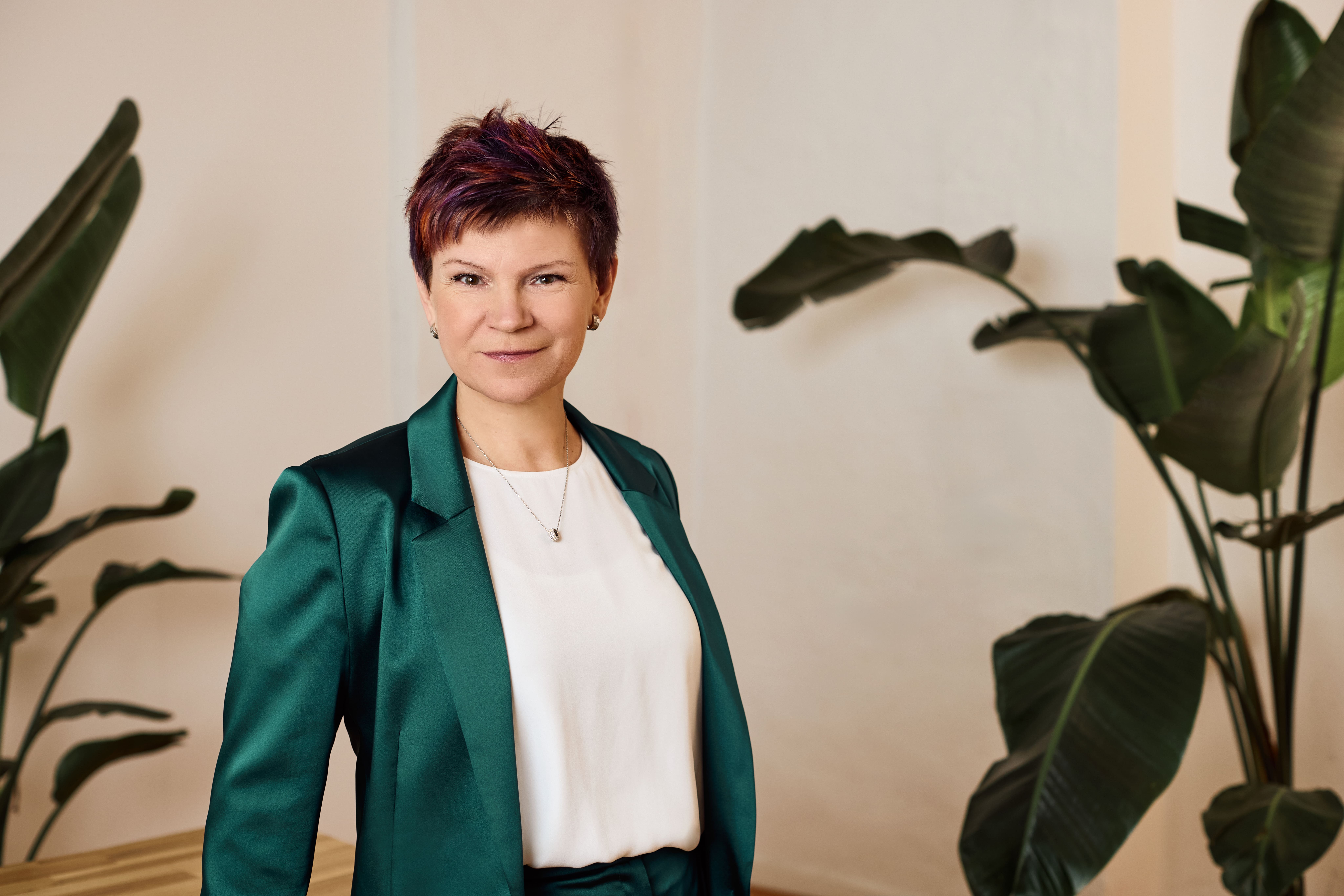 a woman in a green suit and white shirt is standing in front of a plant .
