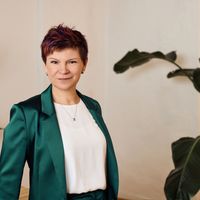 a woman in a green suit and white shirt is standing in front of a plant .