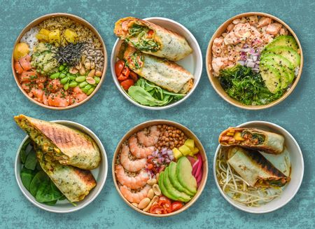Six diverse healthy food bowls and wraps on a blue background. A green banner reads "MENOS DESPERDICIO. MÁS HEALTHY." (Less Waste. More Healthy.).