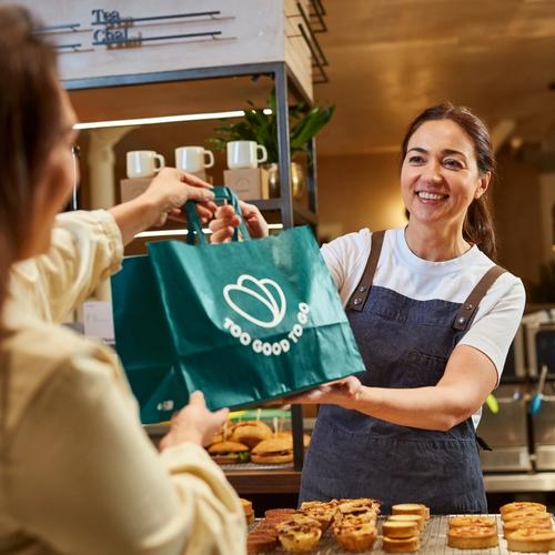 a woman is giving a bag of food to another woman in a bakery .
