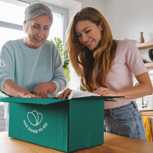 an elderly woman and a young woman are opening a box in a kitchen .
