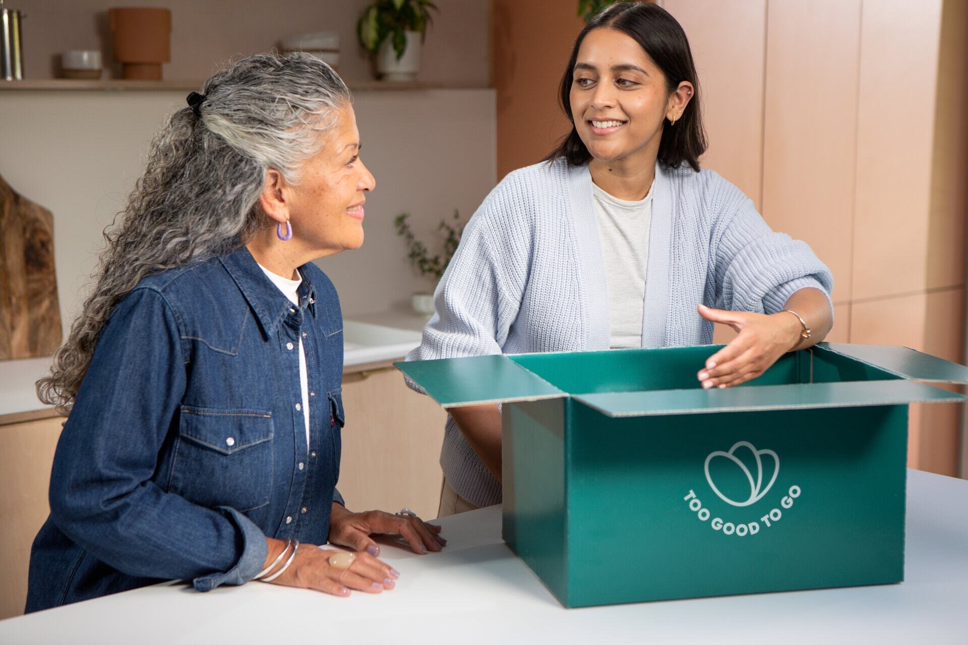 two women are sitting at a table with a box on it .