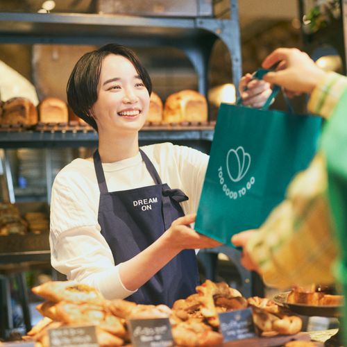 a woman using a tablet next to a bag that says too good to go