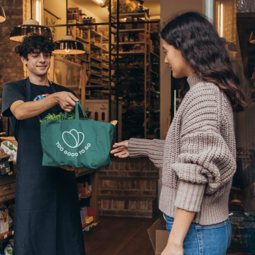 a man holding a green bag that says too good to go