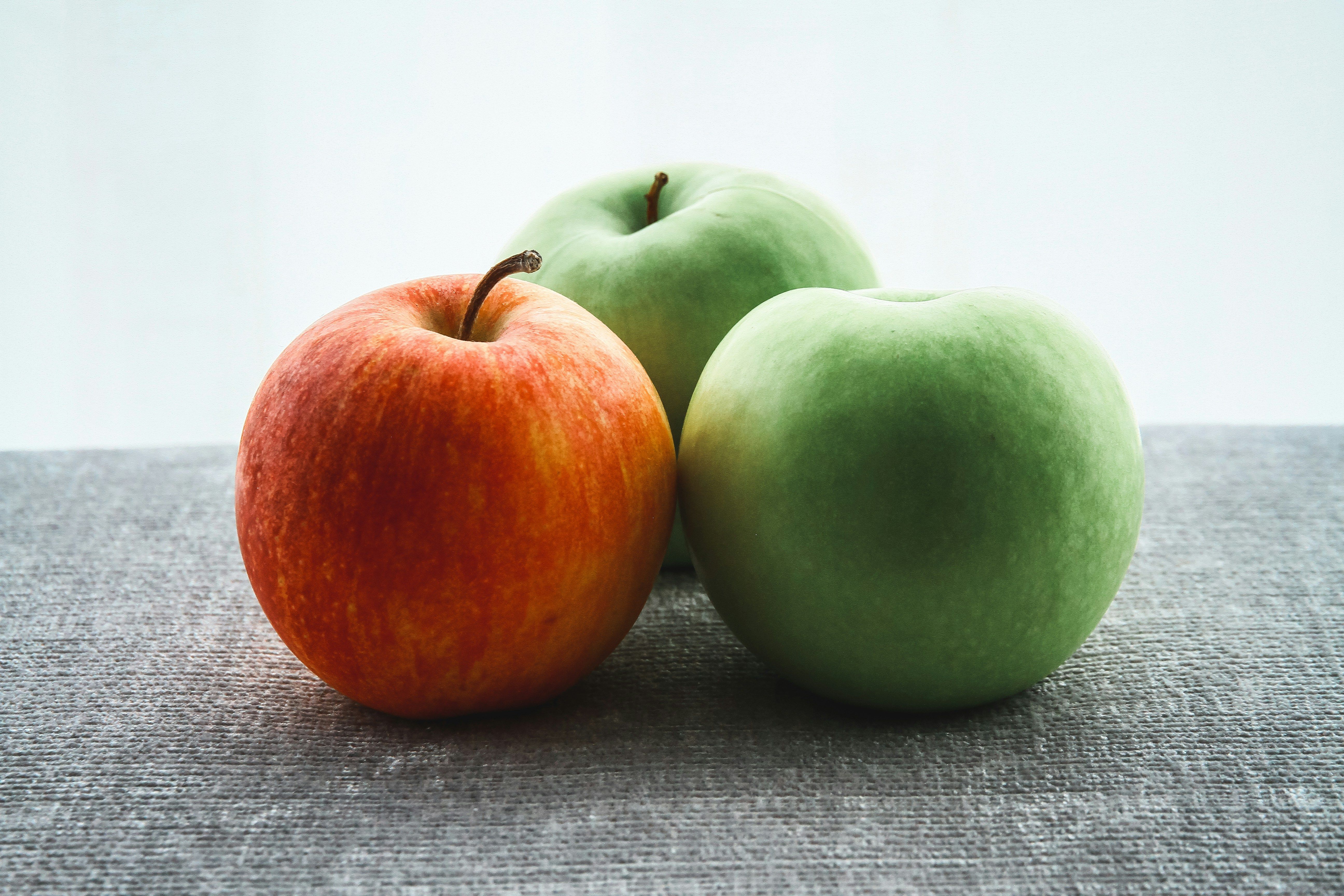 three apples , one red and two green , are sitting on a table .