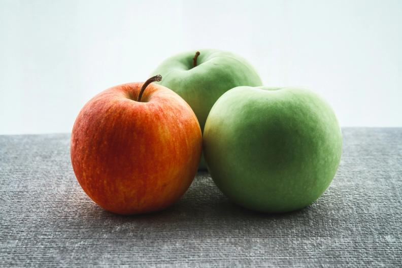 three apples , one red and two green , are sitting on a table .