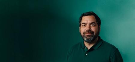 a man with a beard wearing a green polo shirt is standing in front of a green wall .