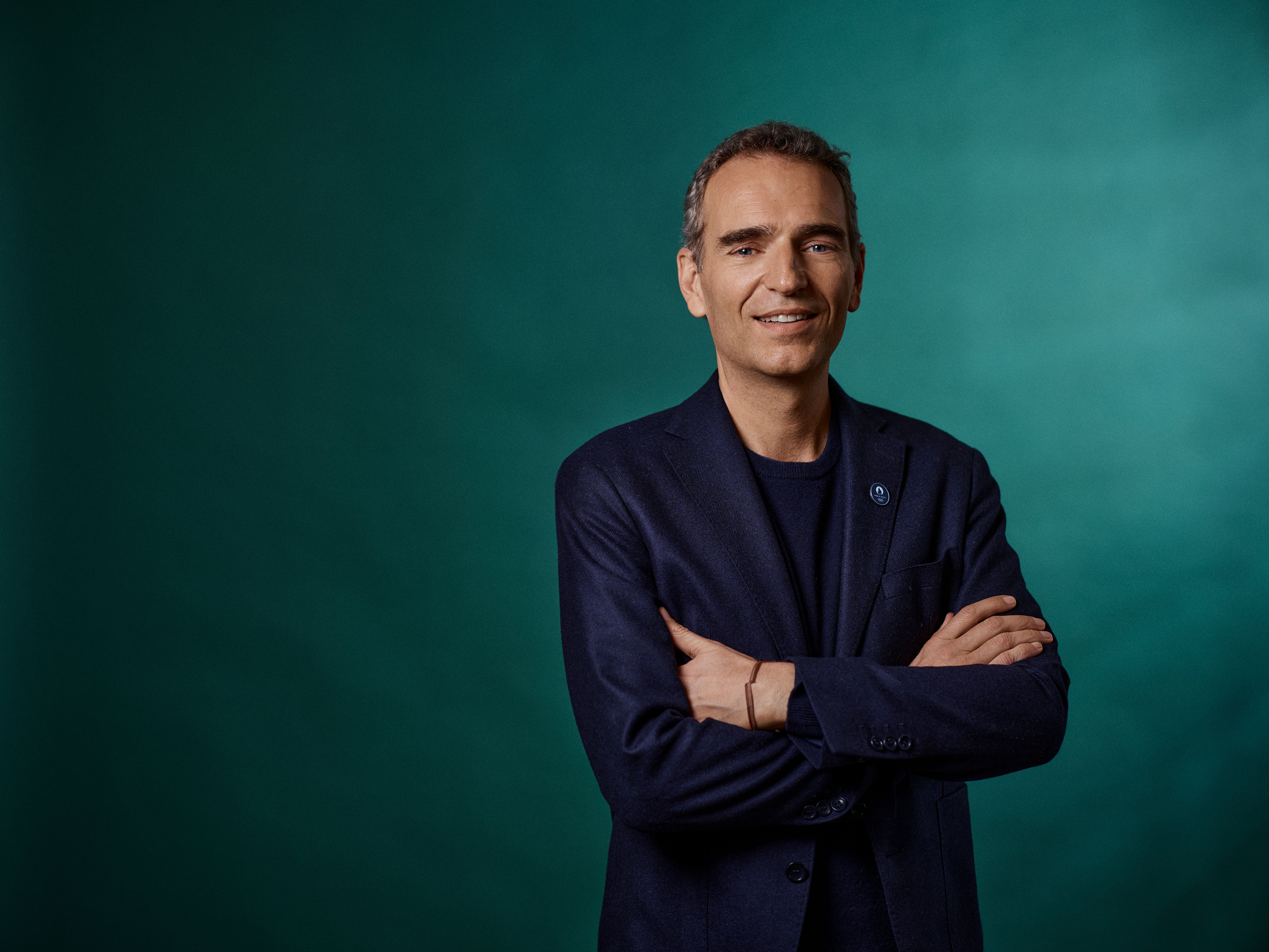 a man in a suit is standing with his arms crossed and smiling .