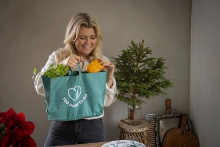 a woman is holding a green bag filled with vegetables .