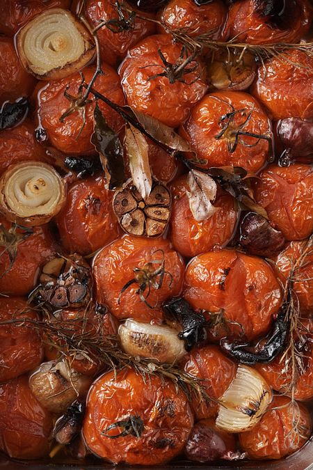 Roasted tomatoes, halved onions, and garlic with rosemary and bay leaves in a liquid.