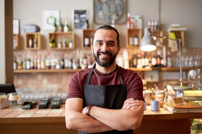 Un barista souriant se tient devant son comptoir les bras croisés