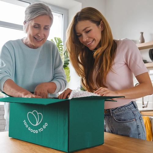 an elderly woman and a young woman are opening a box in a kitchen .