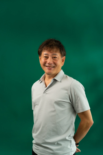 a man in a grey shirt is smiling in front of a green background