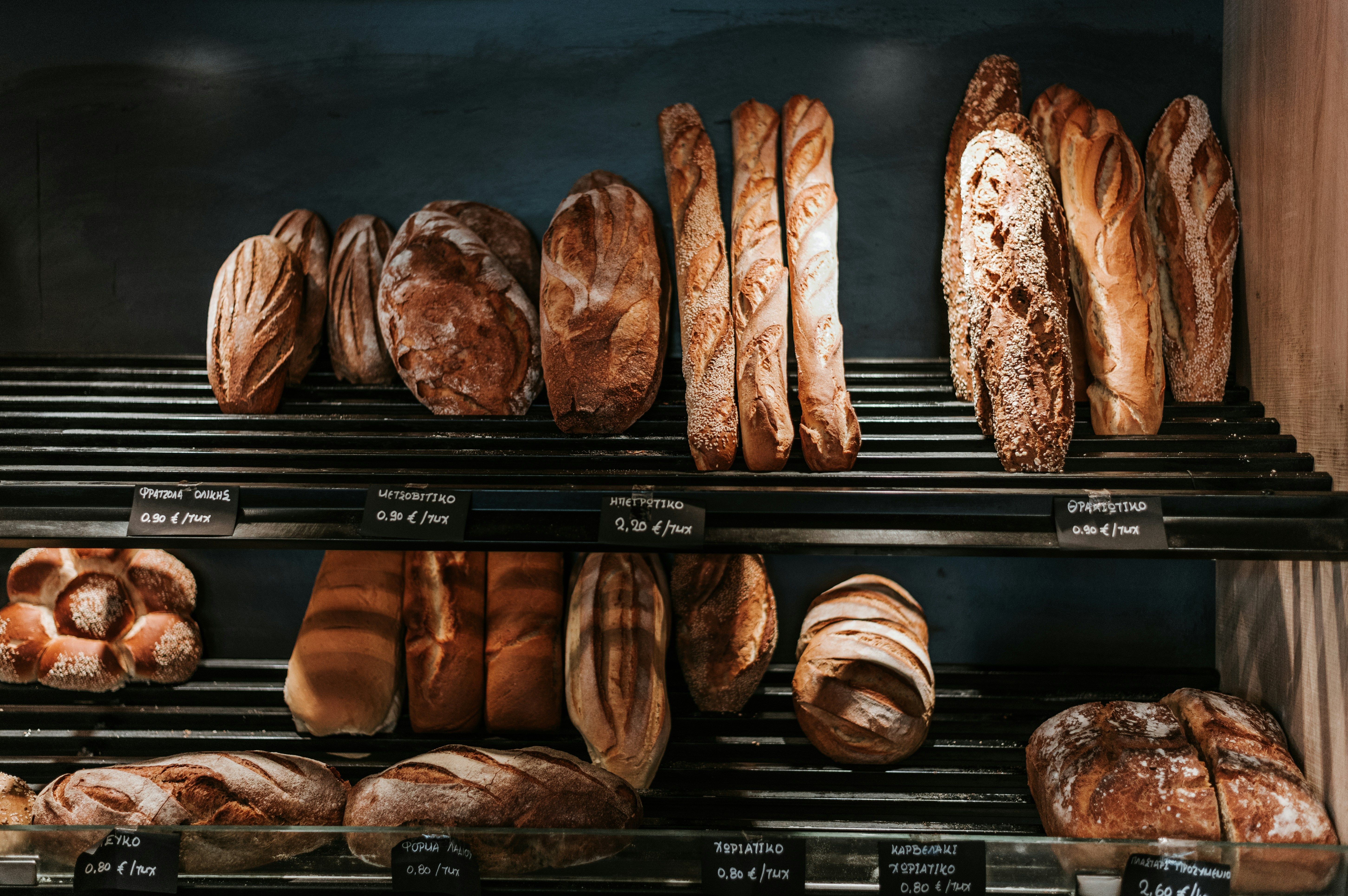 a variety of breads are displayed on a shelf in a bakery .