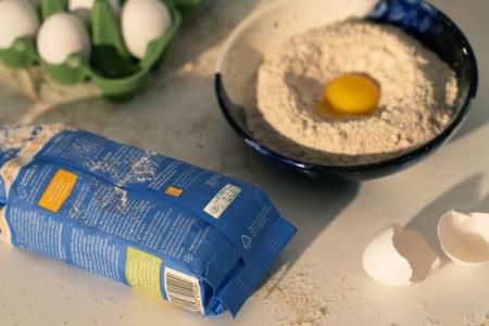 a bag of flour is sitting on a table next to a bowl of flour and an egg .