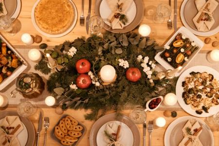 Overhead view of a festive dining table set with a greenery centerpiece, lit candles, multiple food dishes, and place settings.