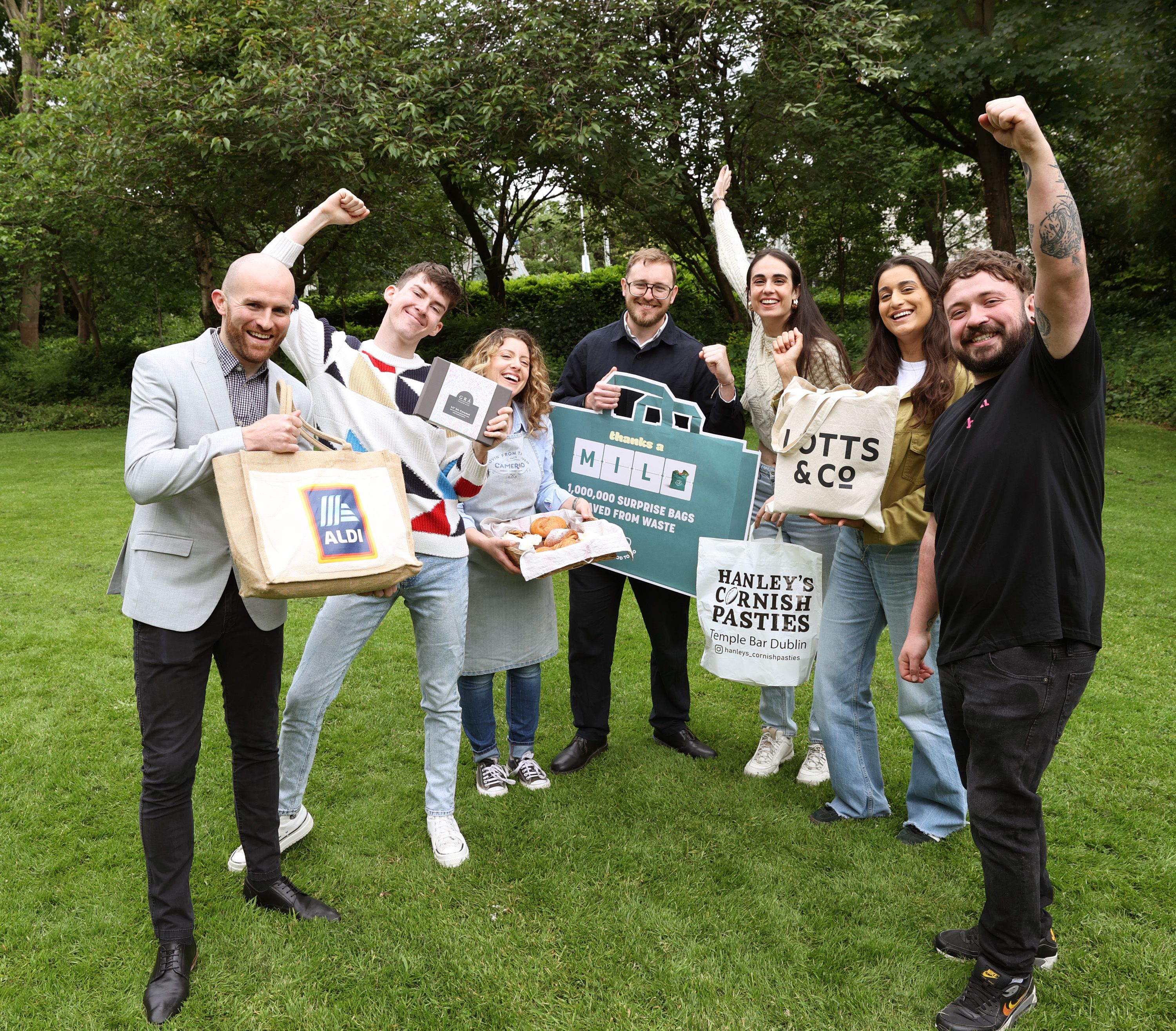 a group of people standing on top of a lush green field holding Surprise Bags.