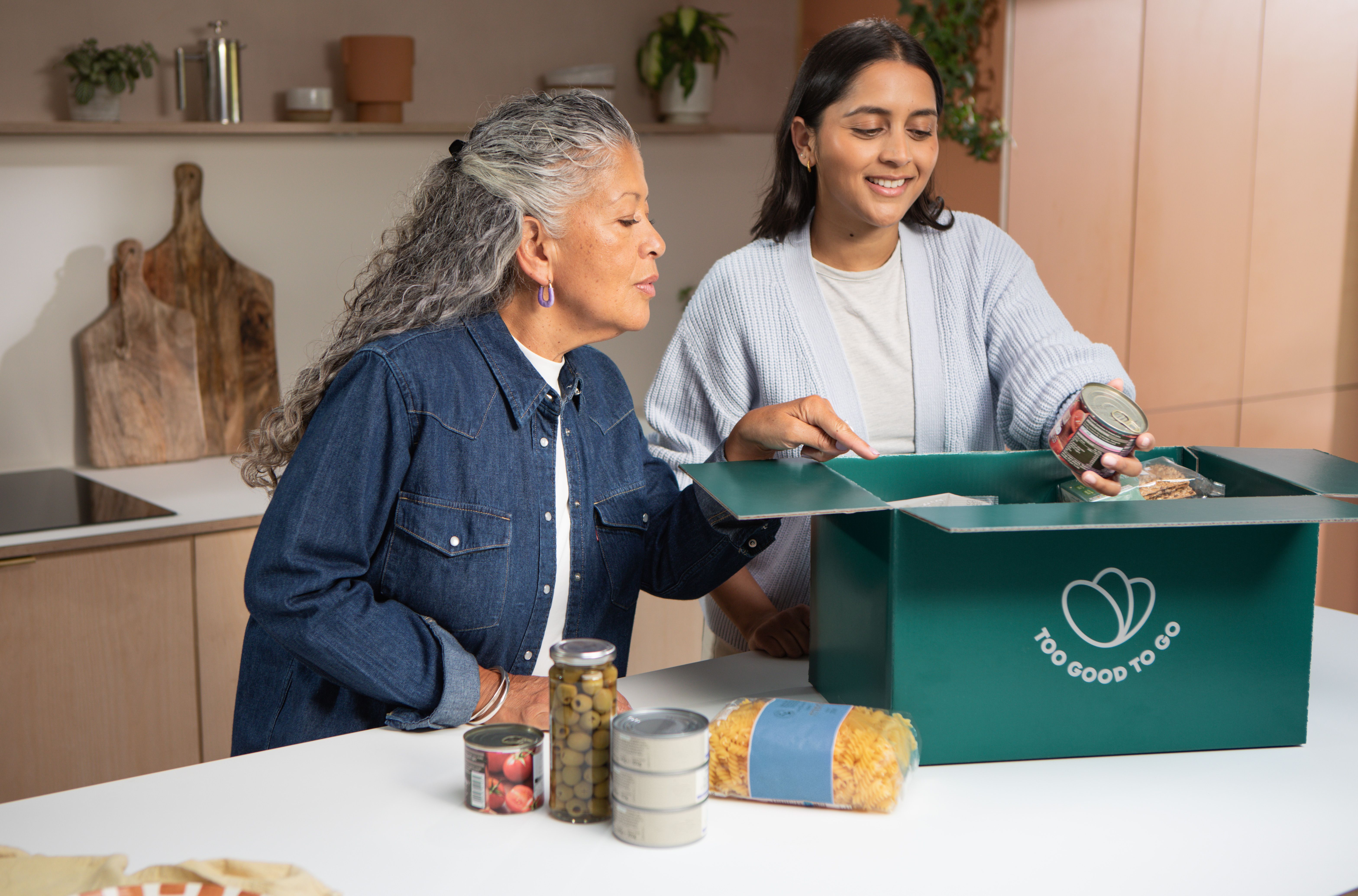 a woman is helping an older woman open a box of food .