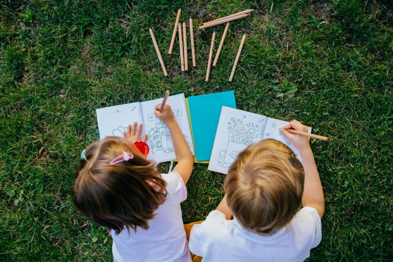 a boy and a girl are sitting on the grass drawing with pencils .