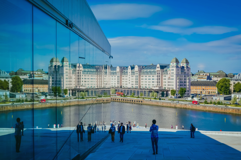 a group of people walking in front of a large building overlooking a body of water