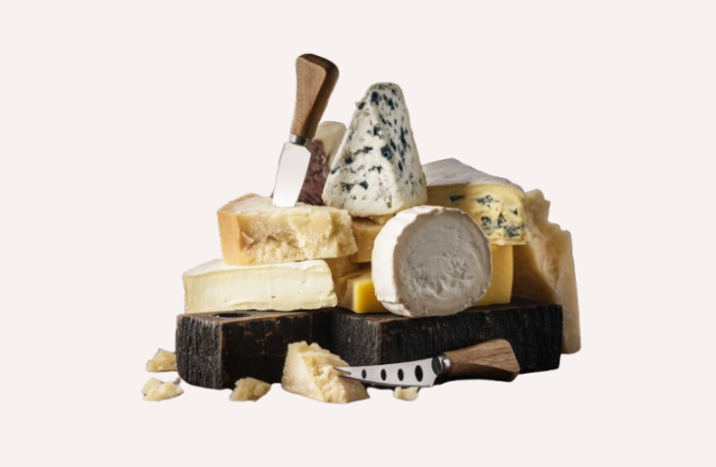 A selection of cheeses including blue cheese, brie, and hard cheeses, with two cheese knives on a dark cutting board.