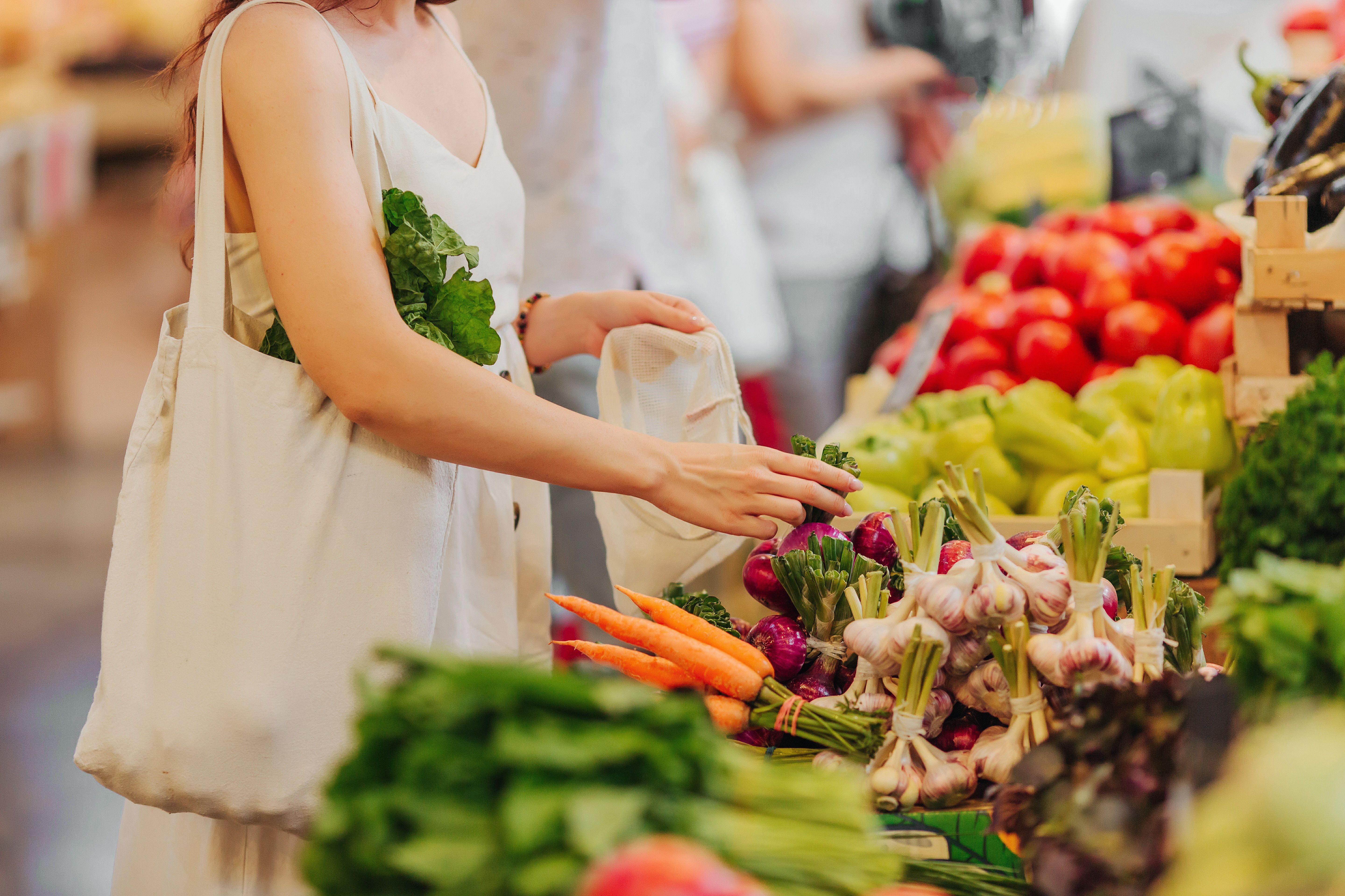 A woman with a reusable bag selects fresh produce at a market.