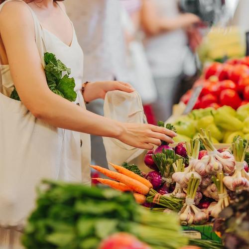 A woman with a reusable bag selects fresh produce at a market.