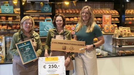 Three smiling women in a bakery hold a plaque celebrating "2 million meals saved" and a €250 donation voucher.