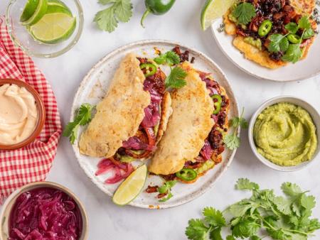 Tacos and a tostada with guacamole, pickled red onions, and a dark filling, surrounded by sauces, limes, and cilantro.