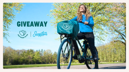 Smiling woman on a bicycle with a 'Too Good To Go' branded basket cover in a sunny park. 'GIVEAWAY' text, Too Good To Go and Swapfiets logos are visible.