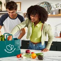 a man and a woman are standing in a kitchen holding a bag of vegetables .