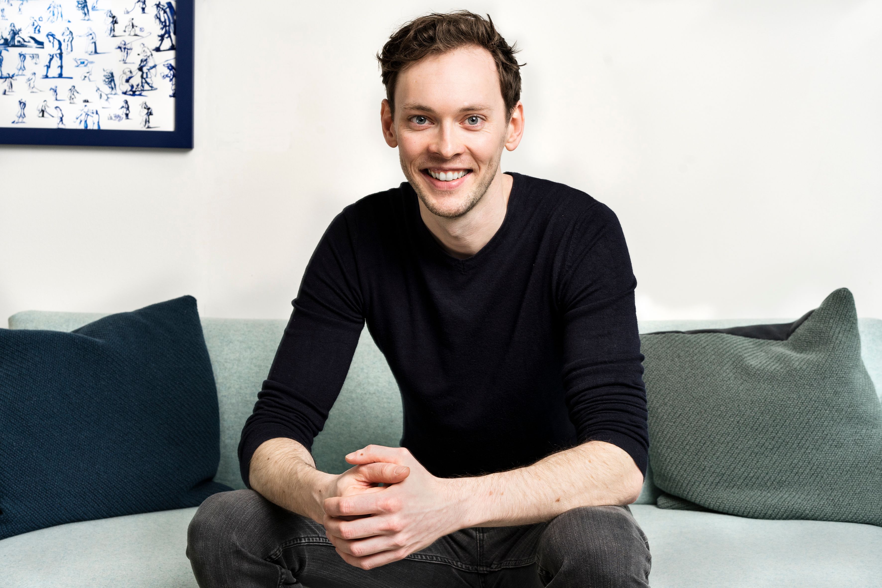 a man is sitting on a couch with his hands folded and smiling .