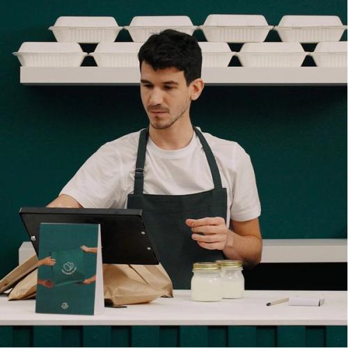 a man in an apron is sitting at a counter using a tablet computer .