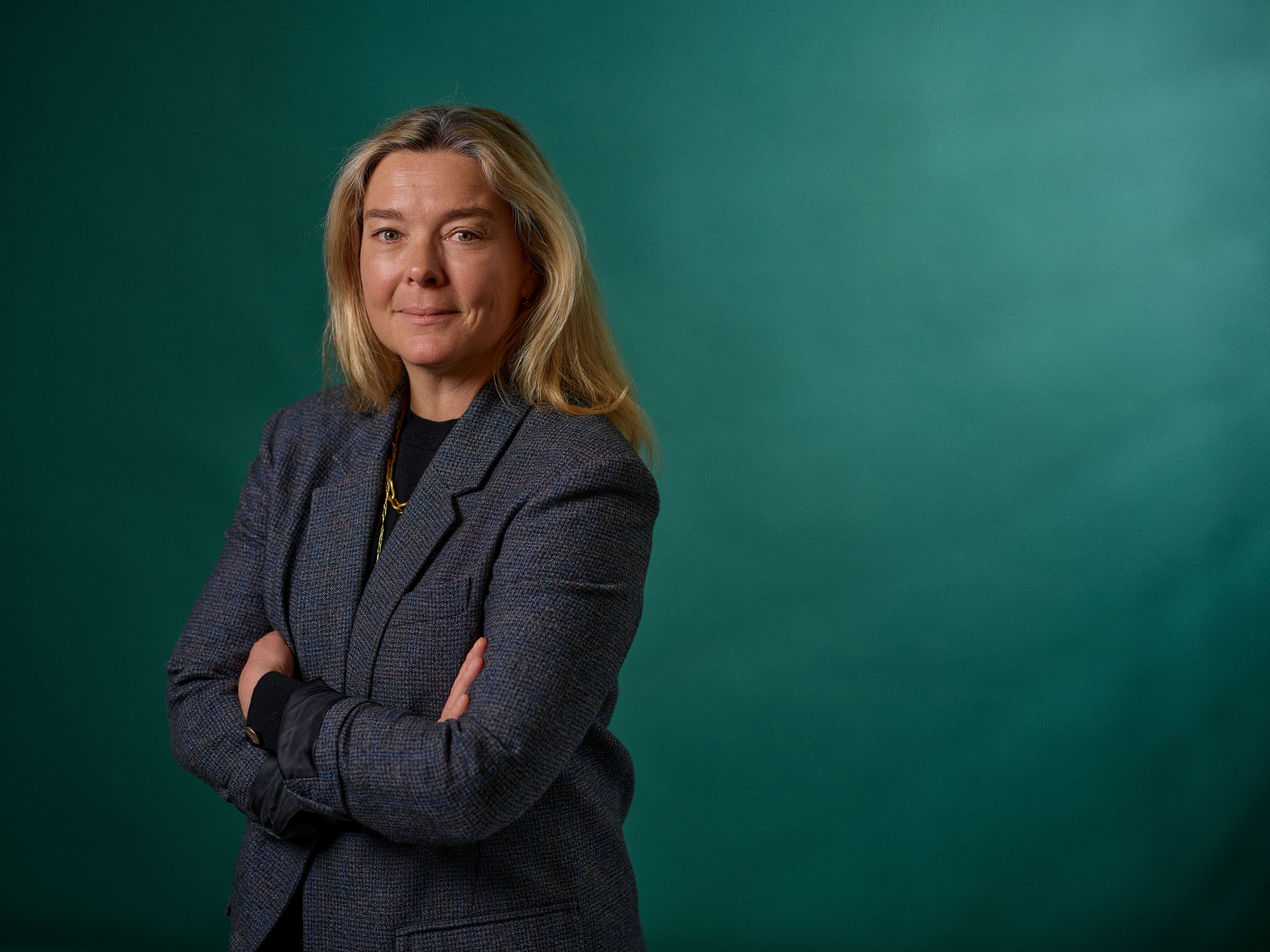 a woman in a suit is standing with her arms crossed in front of a green background .