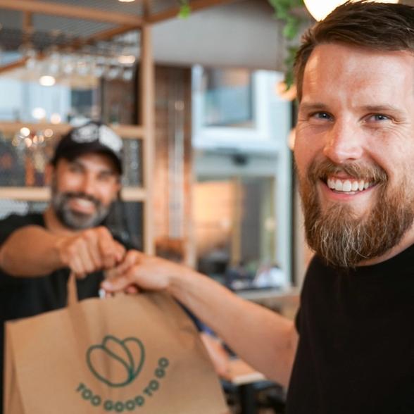 a man with a beard is giving a bag to another man in a restaurant .