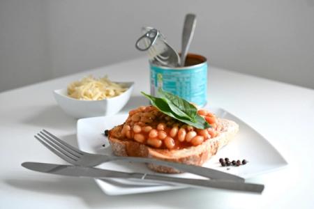 A plate of baked beans on toast with a can of beans in the background.