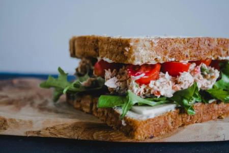 A sandwich with tuna, tomatoes, lettuce and mayonnaise on a wooden cutting board.