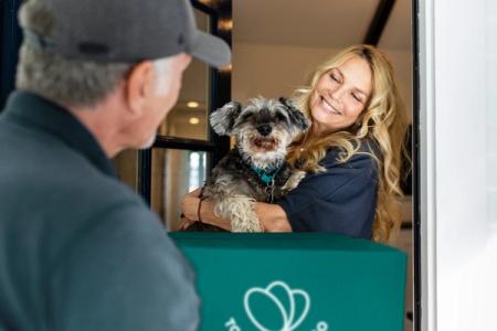 a woman is holding a small dog and smiling at a delivery man .