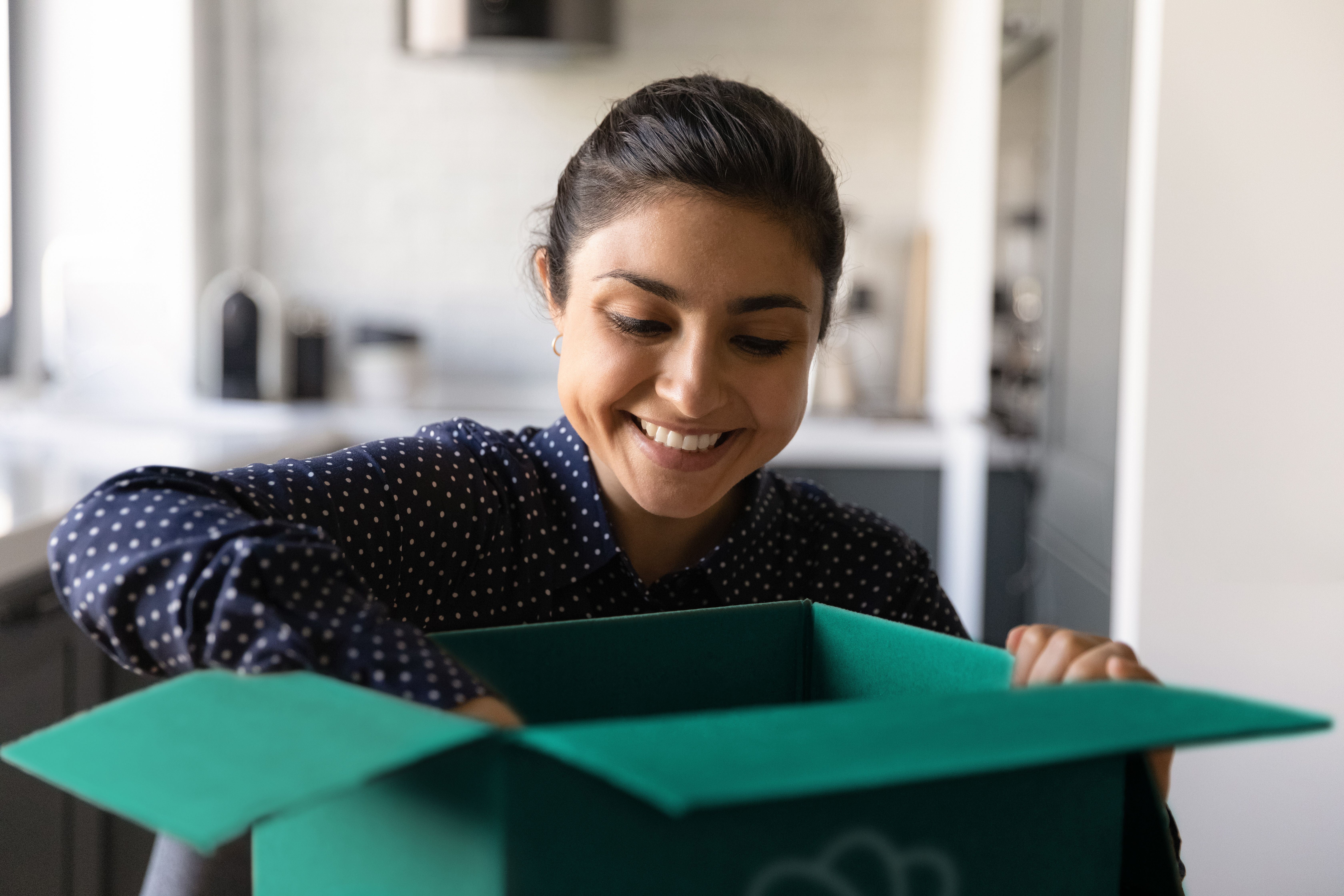 Una mujer tiene una Caja Despensa Too Good To Go frente a ella y está mirando el contenido que le ha venido en el envío