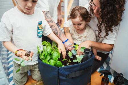 a woman and two children are planting plants in a pot- A Bruga