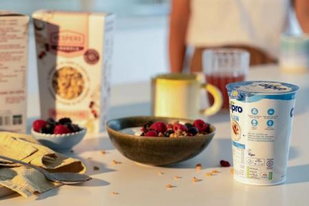 A bowl of cereal and a cup of yogurt are on a table.