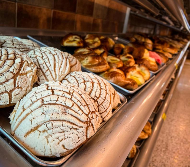 A bakery display of Mexican sweet breads, with conchas in the foreground.